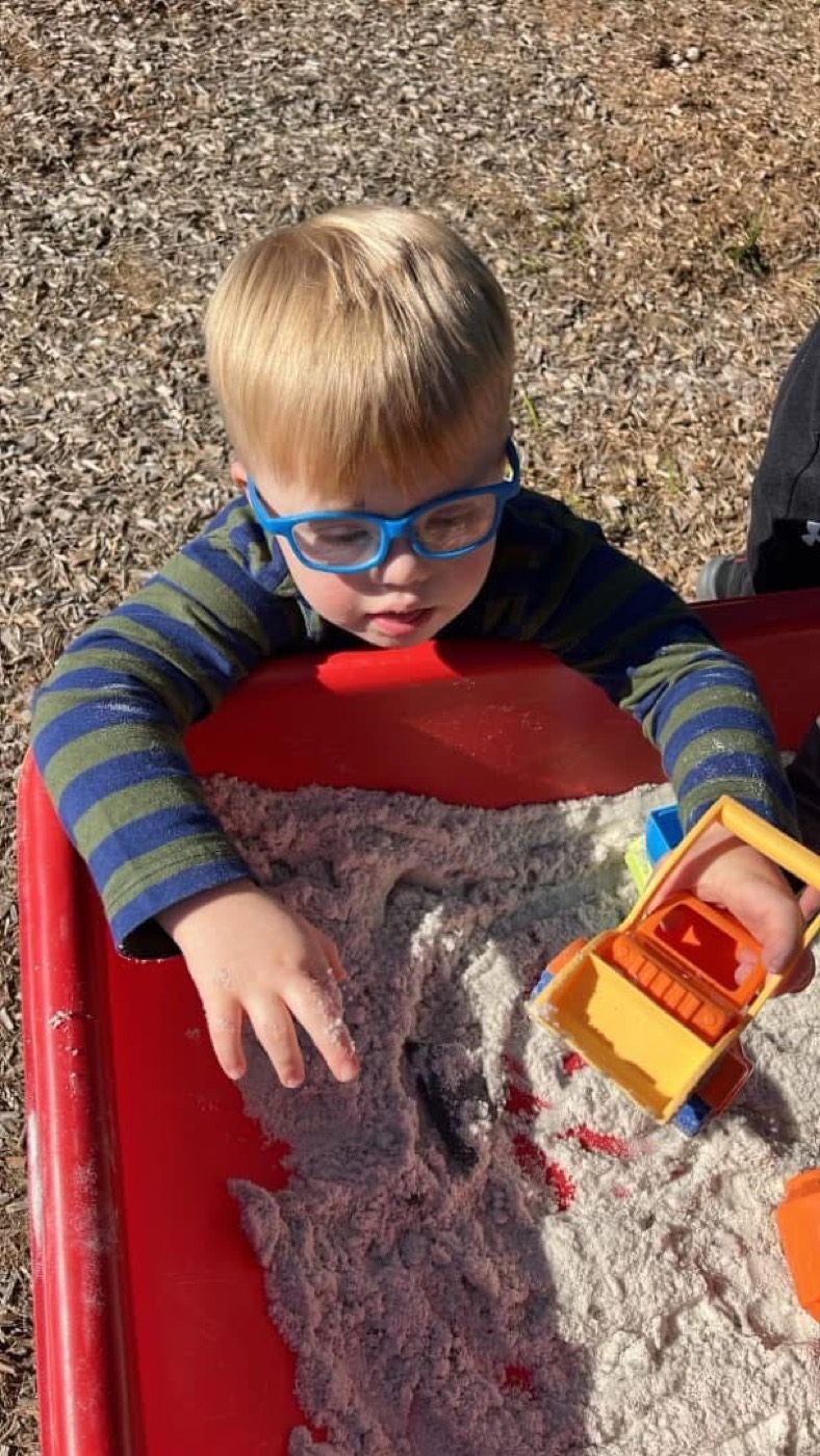 A boy digging with a toy dump truck at the outdoor sand table