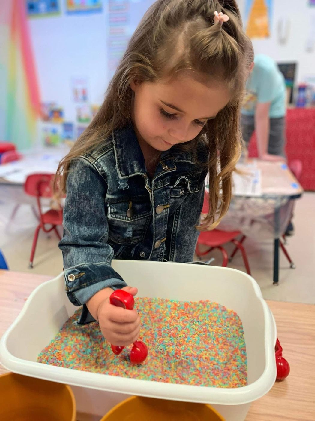 A girl scooping rainbow sensory rice in the classroom